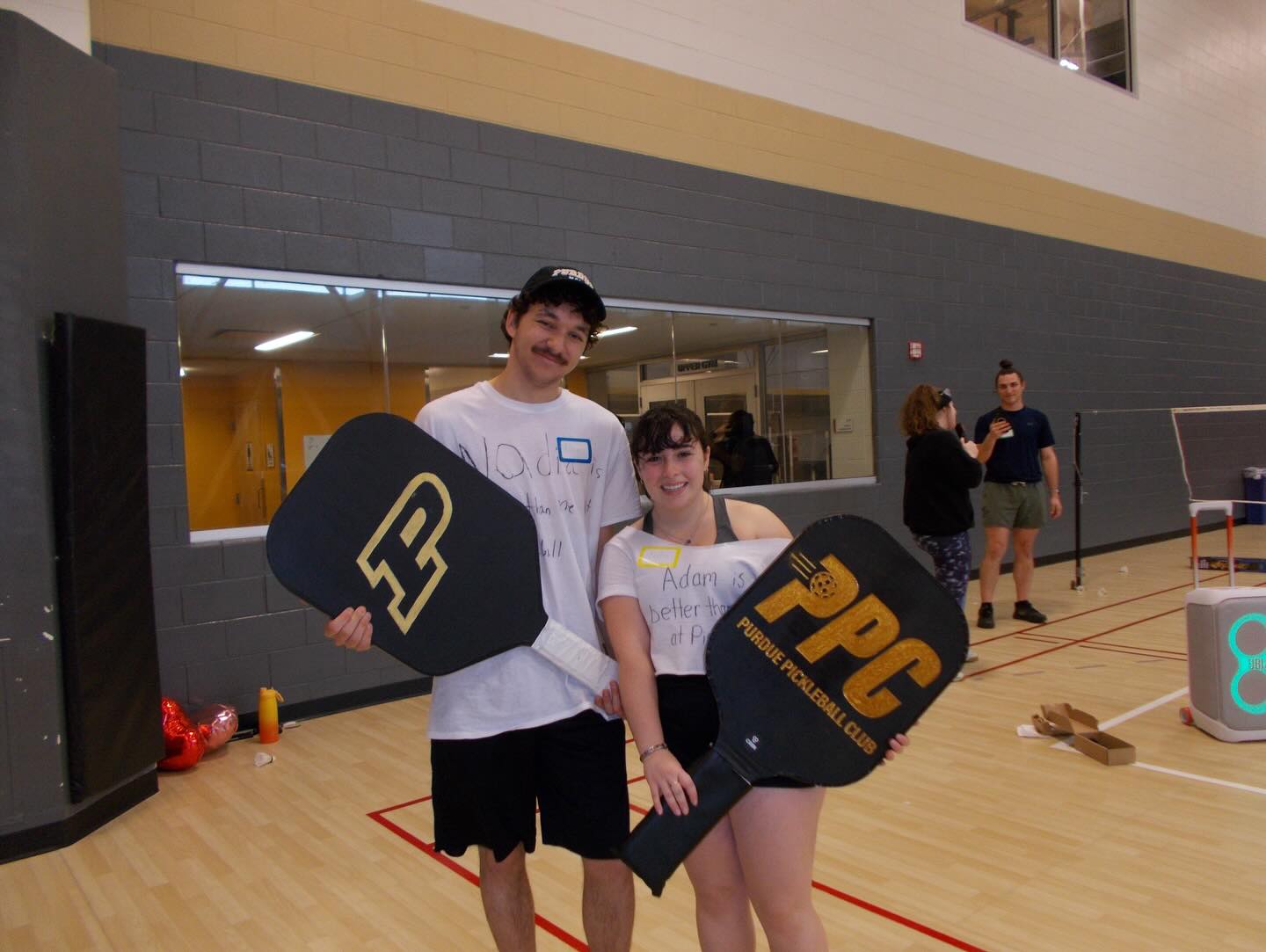 Two players holding Purdue Pickleball Club paddles